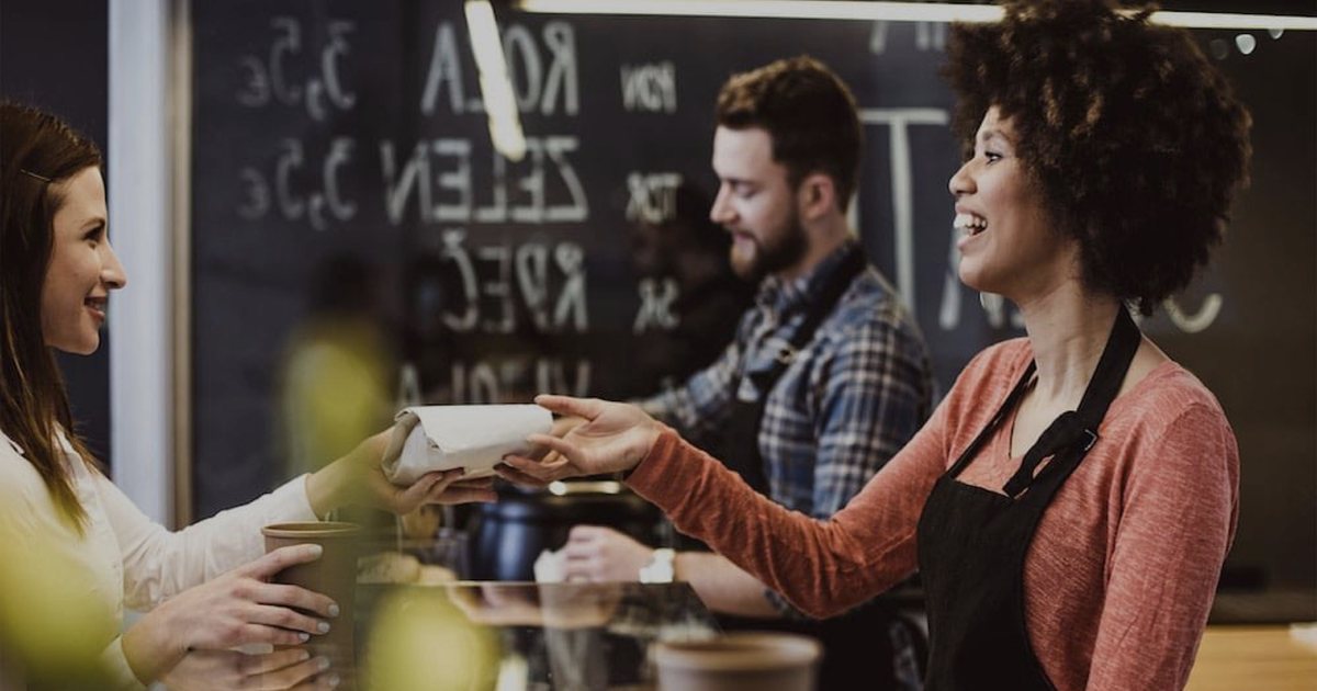A café worker handing a customer her order