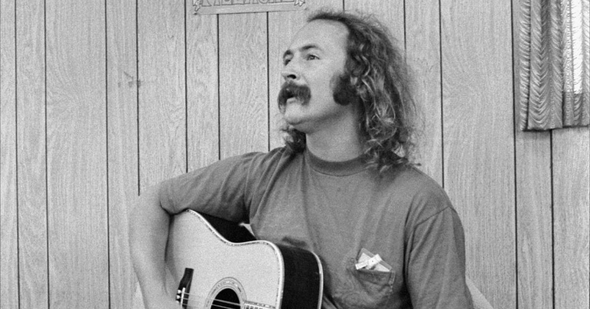 David Crosby playing an acoustic guitar beneath a Byrds Fillmore poster